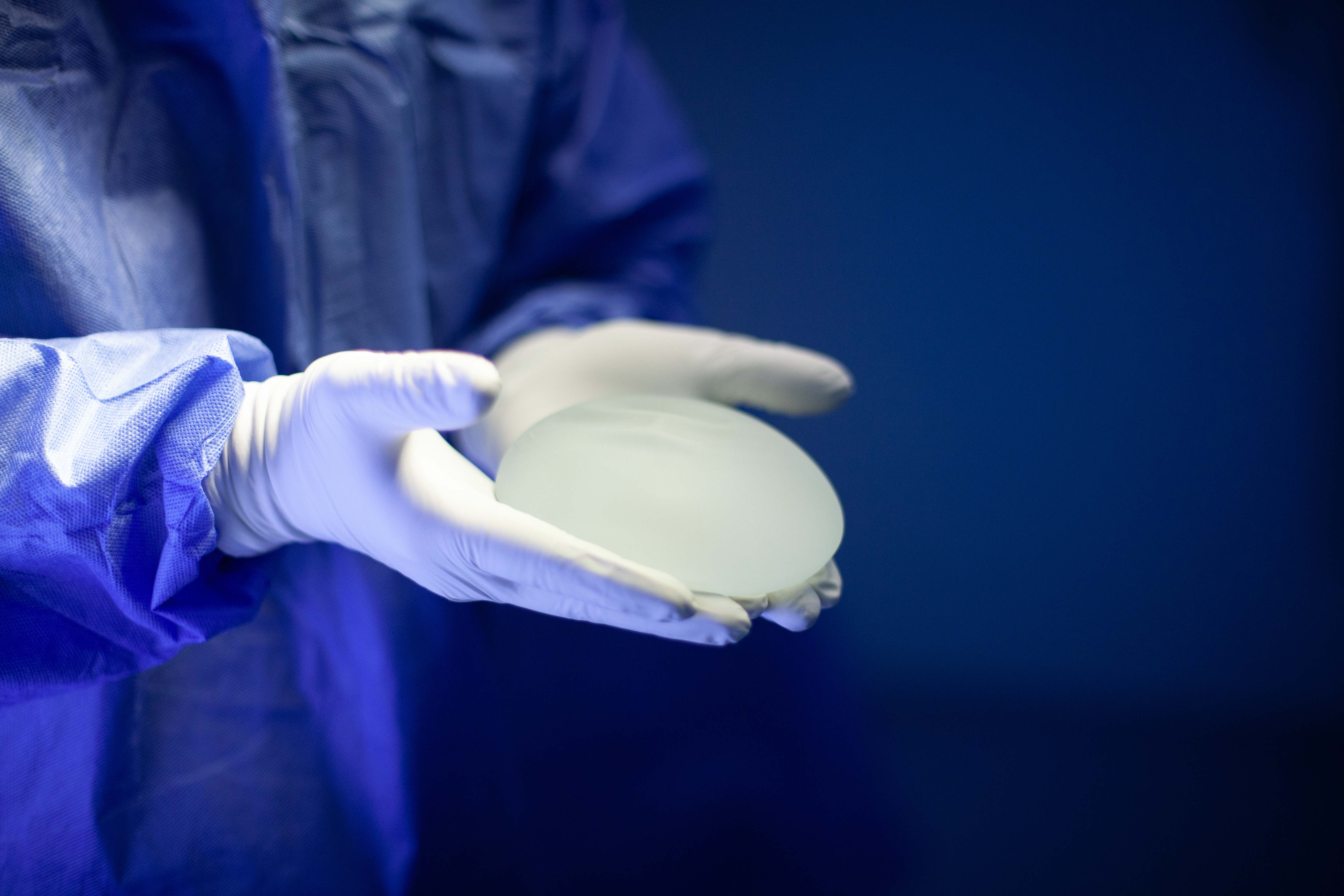 operatiekamersetting met alleen handen in beeld van chirurg die met latexhandschoenen aan een borstimplantaat in beide handen toont aan de camera