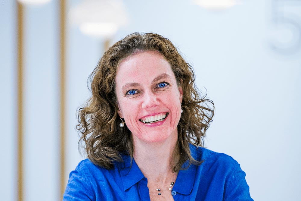 portretfoto van Sandra, een witte vrouw met bruin krullend haar, ze kijkt lachend de camera in