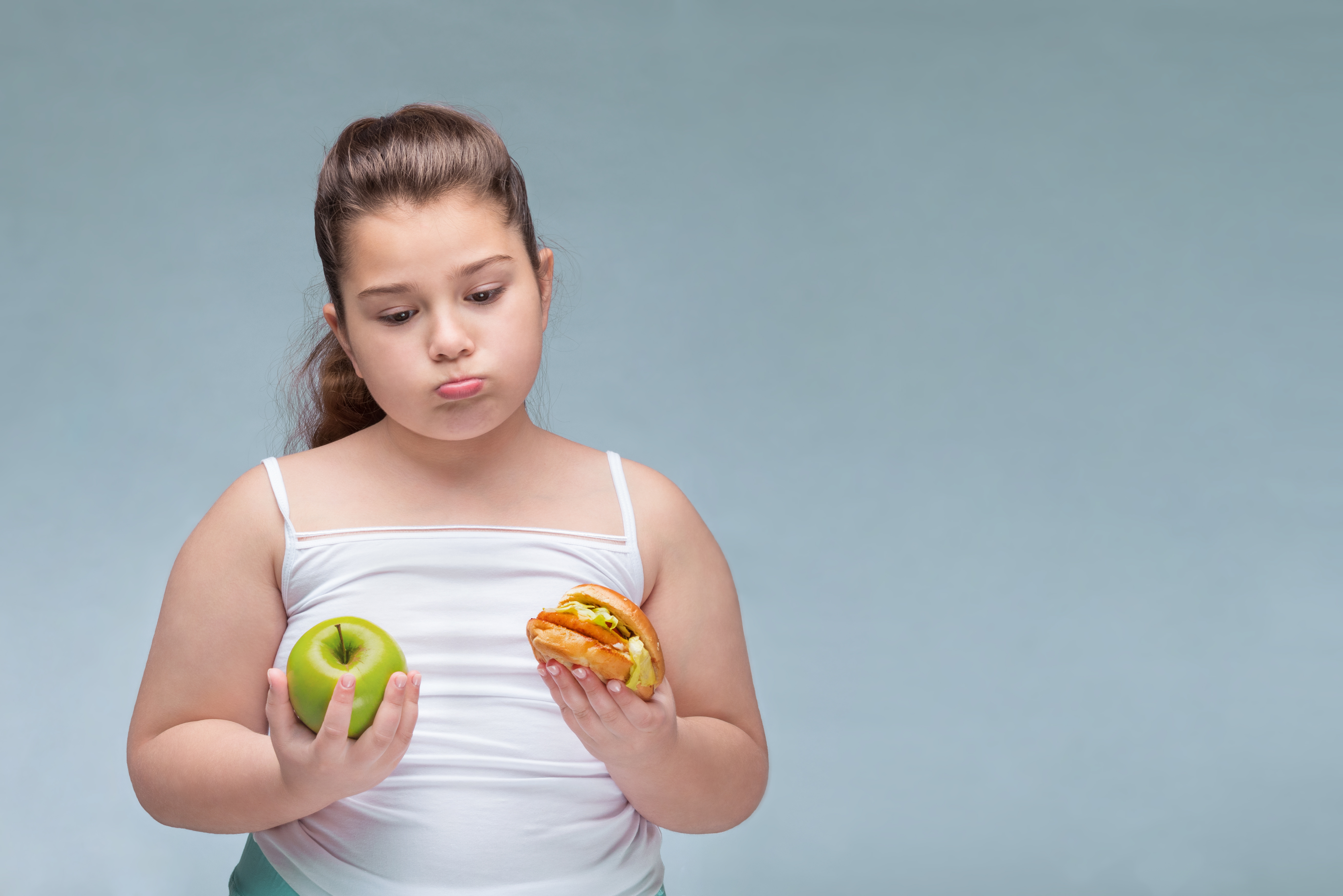 meisje met appel in een hand en hamburger in de andere tegen blauwe achtergrond